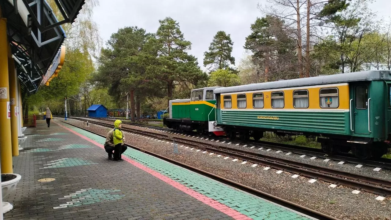 Юный пассажир детской железной дороги смотрит на поезда